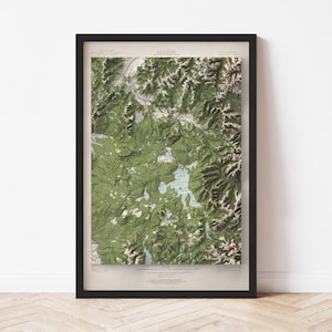 May include: A framed topographic map with a black frame. The map features a detailed, three-dimensional rendering of a mountainous region, with shades of green and brown indicating elevation. The map is a vintage style.
