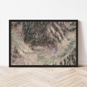 May include: A framed aerial photograph of a mountainous region with a large valley in the center. The photograph is in shades of brown, green, and gray, and shows a variety of landforms, including mountains, valleys, and rivers.