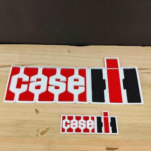 Puede incluir: Dos parches bordados con el logotipo de Case IH. El diseño consiste en la palabra "case" en letras blancas sobre un fondo rojo, seguida de una "IH" estilizada en negro y rojo. Los parches tienen un borde blanco y son rectangulares.