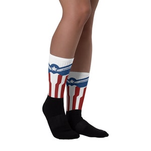 May include: A pair of white socks with red and blue stripes and a star and wings design. The socks are black at the toes and heels.