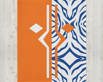 May include: A throw blanket with a geometric design in orange, white and blue. One side features a white and blue zebra print, while the other side has a geometric pattern with a white diamond shape.