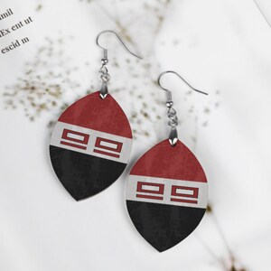 Può includere: Un paio di orecchini pendenti con un design rosso, bianco e nero. Gli orecchini hanno la forma di una lacrima e un gancio argentato.