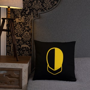 Puede incluir: Almohada de color negro y amarillo con un diseño geométrico. La almohada está sobre una cama gris con una cabecera negra.