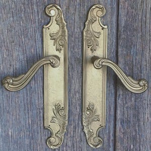 Una coppia di eleganti maniglie e placche per porte in bronzo massiccio in stile rococò, recuperate da un edificio storico.