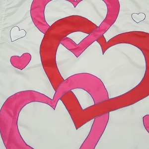 May include: White fabric with a pattern of overlapping hearts in shades of red and pink. Outlined in purple, the hearts create a romantic design. Smaller hearts are scattered across the background.