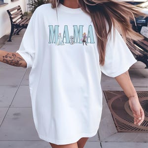 Pode incluir: Camiseta branca oversized com uma estampa gráfica azul da palavra "MAMA" com personagens do filme Frozen.