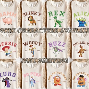 Puede incluir: Una colecci&oacute;n de camisetas beige con nombres de personajes de dibujos animados en letras de estilo universitario. Cada camiseta muestra un personaje diferente, como Hamm, Slinky, Rex y Alien, con el a&ntilde;o "1995" debajo. Tambi&eacute;n se ve el texto "MORE CHARACTERS AVAILABLE!".