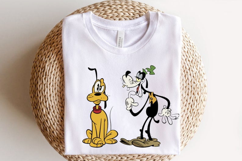May include: White t-shirt with a cartoon image of Pluto and Goofy. Pluto is a yellow dog sitting down and Goofy is a black and white dog standing up.