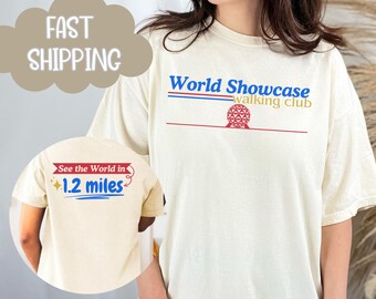 May include: A white t-shirt with the text "World Showcase walking club" and a graphic of the Spaceship Earth ride. The back of the shirt has the text "See the World in 1.2 miles" with a star and a red ribbon.
