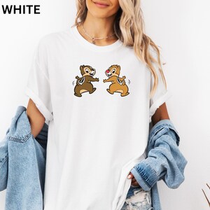 May include: White t-shirt featuring a cartoon graphic of two chipmunks. The chipmunks are brown and tan, with one having a red nose. The word "WHITE" is printed in bold, black letters at the top left of the shirt.