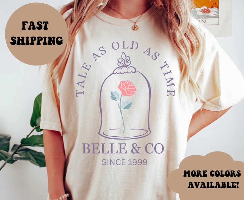 Peut inclure: Un t-shirt cr&egrave;me avec un graphique violet d'une rose dans un d&ocirc;me de verre. Le texte "Tale as old as time" est &eacute;crit autour du d&ocirc;me et "Belle & Co. Since 1999" est &eacute;crit sous le d&ocirc;me.