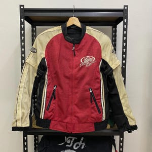 Può includere: Giacca da moto rossa, nera e crema con chiusura a zip e le parole "Speed Demon" ricamate sul davanti.