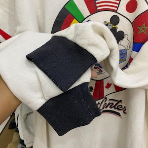 May include: Cream-colored sweatshirt with black cuffs. The design features Mickey Mouse, flags, and the words "Winter Center" in red script. The sweatshirt has a vintage aesthetic.