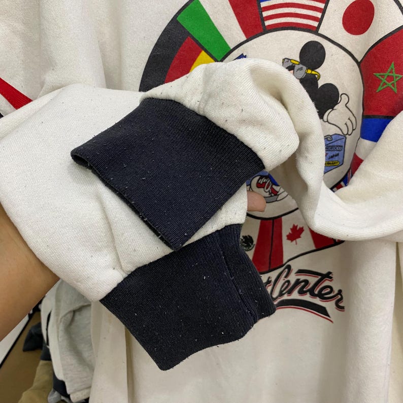 May include: Cream-colored sweatshirt with black cuffs. The design features Mickey Mouse, flags, and the words "Winter Center" in red script. The sweatshirt has a vintage aesthetic.