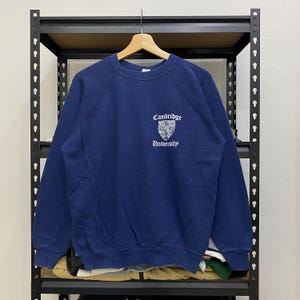 May include: A navy blue sweatshirt with a white embroidered crest and the text "Cambridge University".