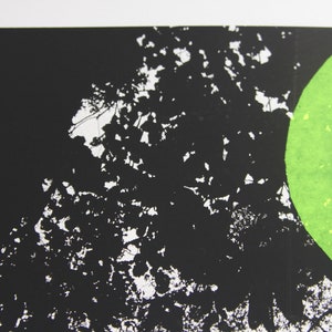 May include: A black and white print featuring a green circle with a white circle inside. The background is black with white splatter paint.