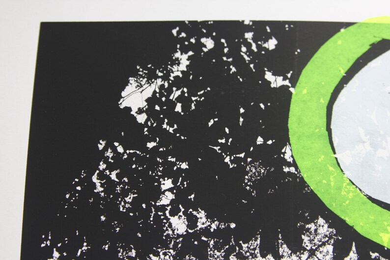 May include: A black and white print featuring a green circle with a white circle inside. The background is black with white splatter paint.