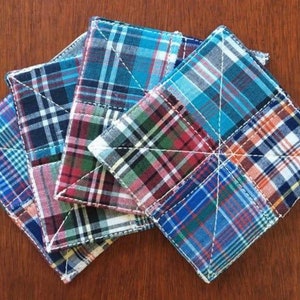 Op de afbeelding: Vier handgemaakte, gestikte onderzetters gemaakt van patchwork-stof in tinten blauw, rood en wit. De onderzetters hebben een ruitpatroon en zijn perfect om elke woning een vleugje rustieke charme te geven.