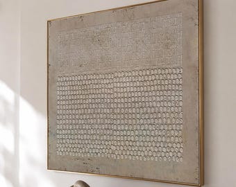 May include: A large square wall art piece featuring a textured beige and off-white surface with a geometric pattern of vertical lines on the top half and a grid of small raised circular shapes on the bottom half, framed in a thin gold metal frame.