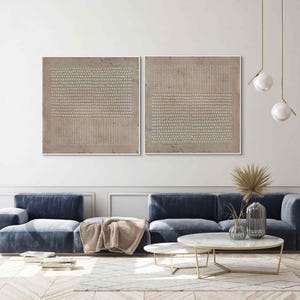 Puede incluir: Dos obras de arte abstractas enmarcadas con una paleta de colores neutros. Cada pieza presenta un dise&ntilde;o texturizado con patrones repetidos en beige y blanco roto, creando una est&eacute;tica minimalista. La obra de arte se exhibe sobre un sof&aacute; azul en un sal&oacute;n moderno.