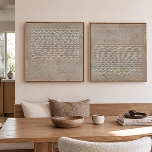 Puede incluir: Dos obras de arte abstractas enmarcadas en tonos neutros. Cada pieza presenta un fondo gris claro texturizado con un patr&oacute;n de peque&ntilde;os puntos y l&iacute;neas blancas. Los marcos son de un c&aacute;lido tono de madera natural. La obra de arte cuelga sobre una mesa de madera.