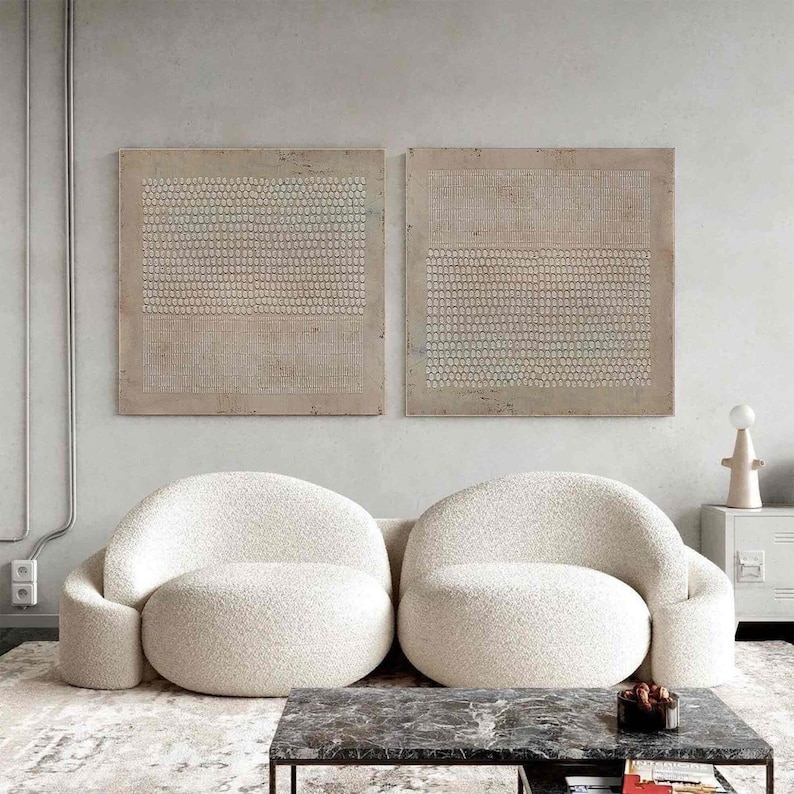Puede incluir: Una moderna sala de estar con dos sillones redondeados color crema y una mesa de centro de m&aacute;rmol oscuro. Dos obras de arte murales abstractas cuelgan sobre las sillas. La habitaci&oacute;n tiene una paleta de colores neutros con una alfombra texturizada.