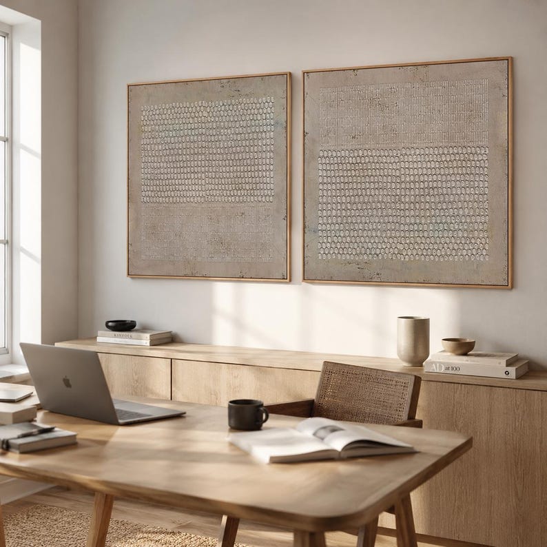Puede incluir: Dos obras de arte abstractas enmarcadas con patrones beige y blancos cuelgan sobre un escritorio de madera. Una computadora port&aacute;til, una taza de caf&eacute; y un libro abierto est&aacute;n sobre el escritorio. Un mueble de madera y una silla de mimbre completan el entorno.