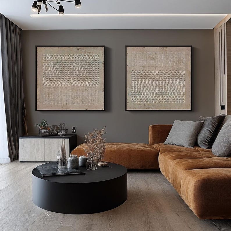 Puede incluir: Dos obras de arte abstractas enmarcadas con un patr&oacute;n beige y blanco cuelgan sobre un sof&aacute; seccional marr&oacute;n. Una mesa de centro redonda negra est&aacute; frente al sof&aacute;. La habitaci&oacute;n tiene un dise&ntilde;o moderno y minimalista.
