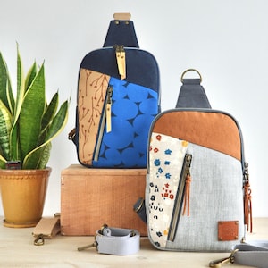 May include: Two sling bags with distinctive patchwork designs. One has a blue and brown pattern, the other a grey, brown, and floral design. Both have zipped pockets, adjustable straps, and leather accents. A potted snake plant is in the background.