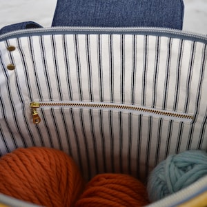 May include: The inside of a yellow striped tote bag with a zippered pocket. The bag is filled with orange and blue yarn.