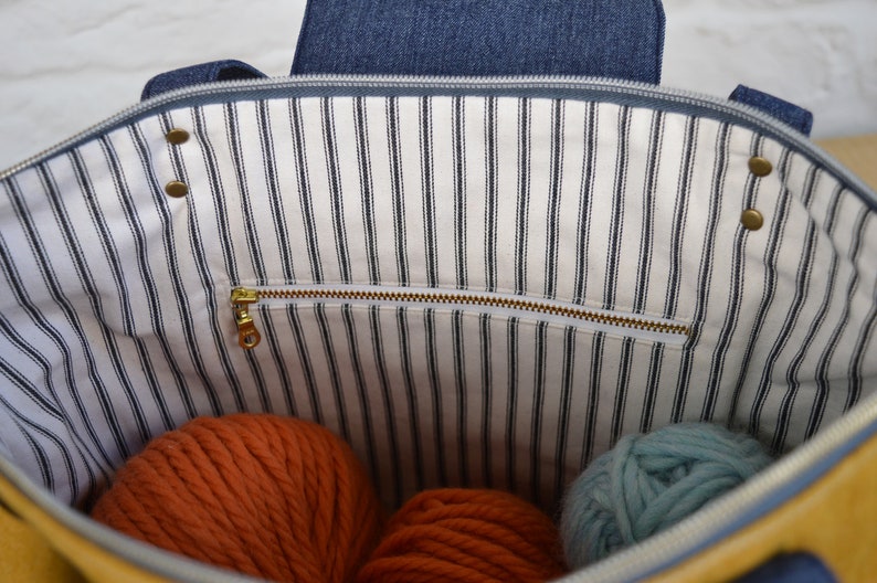 May include: The inside of a yellow striped tote bag with a zippered pocket. The bag is filled with orange and blue yarn.