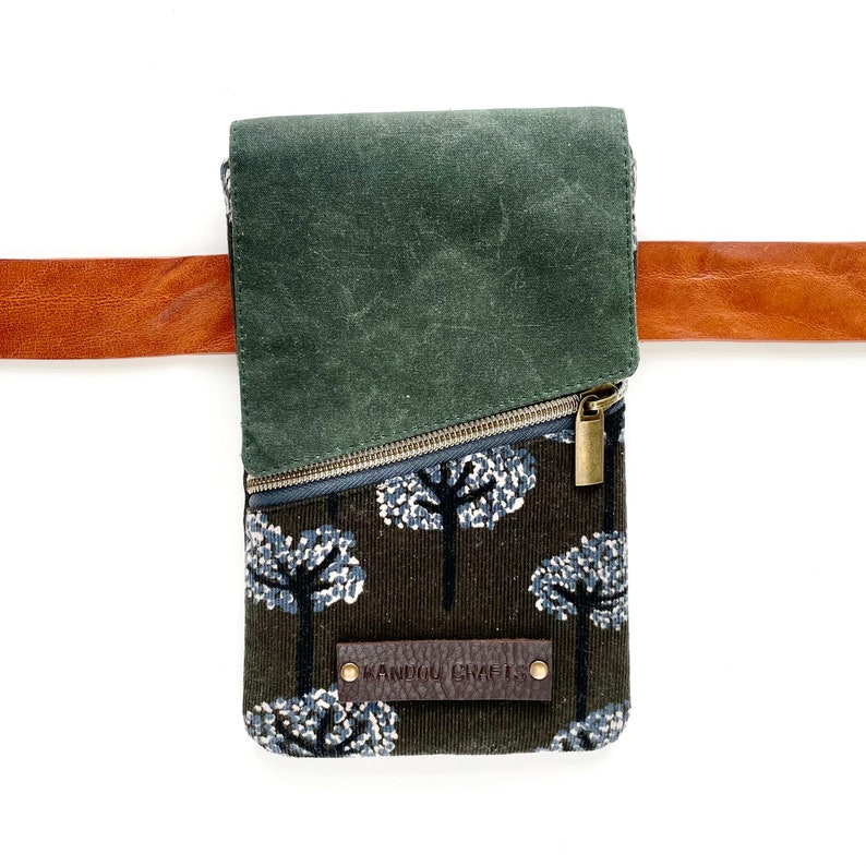 Puede incluir: Un bolso bandolera rectangular con un estampado de bosque y una solapa verde oscuro. El bolso tiene cierre de cremallera y una correa de cuero marr&oacute;n. El texto "KANDOU CRAFTS" est&aacute; en una etiqueta de cuero.
