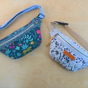 May include: Two fanny packs, one with a green and blue floral print with a leopard, and the other with a white and blue floral print.