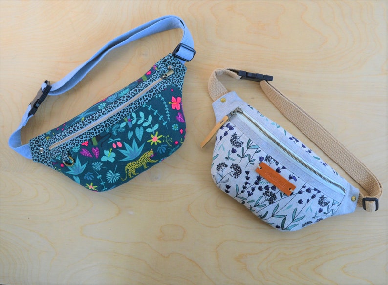 May include: Two fanny packs, one with a green and blue floral print with a leopard, and the other with a white and blue floral print.