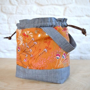 May include: A drawstring bag with a floral print on a mustard yellow background. The bag has a gray denim trim and a brown leather drawstring.