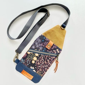 K&ouml;nnte beinhalten: Eine kleine Umh&auml;ngetasche mit Blumenmuster und einer Klappe aus senfgelbem Cord. Die Tasche hat einen Rei&szlig;verschluss und einen braunen Lederriemen mit dem gepr&auml;gten Wort "KANDOU".