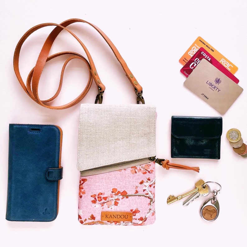 Puede incluir: Un bolso bandolera con la parte superior beige claro y la inferior rosa floral, una correa de cuero marr&oacute;n y un tirador de cremallera de cuero a juego. Tambi&eacute;n se ven una funda de tel&eacute;fono azul, una cartera negra, llaves y tarjetas.