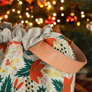Pu&ograve; includere: Una borsa a cordoncino beige con un cinturino in pelle marrone. La borsa &egrave; decorata con un motivo floreale in rosso, verde e oro.