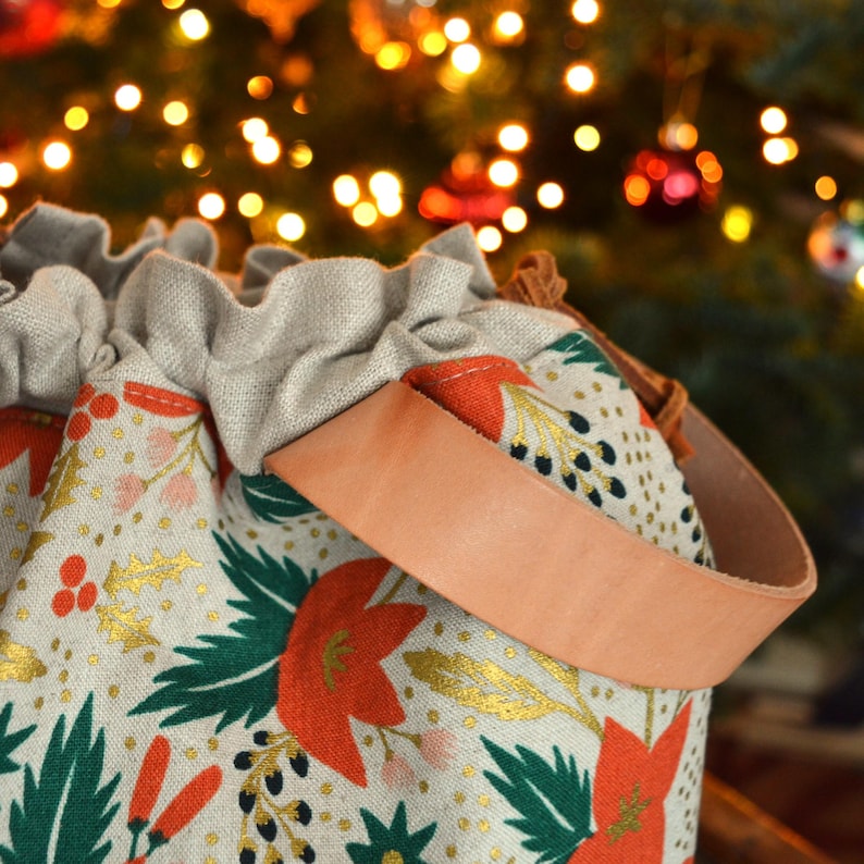 Pu&ograve; includere: Una borsa a cordoncino beige con un cinturino in pelle marrone. La borsa &egrave; decorata con un motivo floreale in rosso, verde e oro.