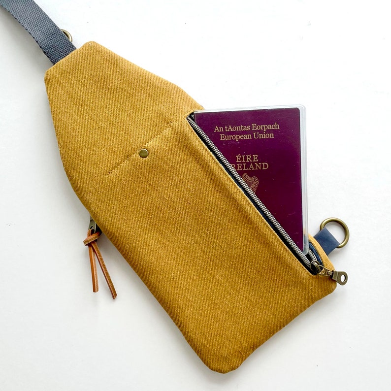 K&ouml;nnte beinhalten: Eine senfgelbe Canvas-Umh&auml;ngetasche mit einer Rei&szlig;verschlusstasche und einem braunen Lederriemen. Die Tasche hat einen Reisepass in der Tasche mit dem Text "An tAontas Eorpach European Union &Eacute;IRE IRELAND".