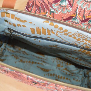 May include: The inside of a tote bag with a blue and gold floral pattern. The bag has a zippered pocket on the inside.