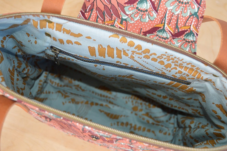 May include: The inside of a tote bag with a blue and gold floral pattern. The bag has a zippered pocket on the inside.