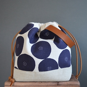 May include: A white drawstring bag with a brown leather strap and a navy blue floral pattern. The bag has a white canvas bottom.