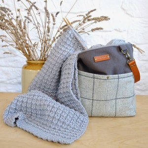 May include: A gray and white plaid tote bag with a brown leather strap and a gray fabric lining. The bag is filled with yarn and a gray knitted scarf.