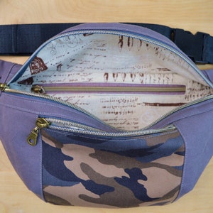 May include: A purple and camouflage fanny pack with a zippered pocket and a zippered closure. The inside of the bag is lined with a cream fabric with a brown and black print.