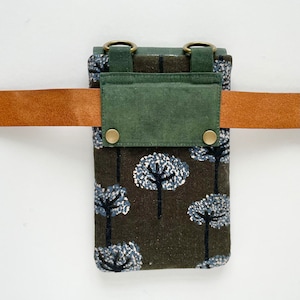 Puede incluir: Peque&ntilde;o bolso rectangular con un estampado de &aacute;rboles marr&oacute;n y azul, una solapa verde y un cintur&oacute;n de cuero marr&oacute;n. El bolso tiene dos anillos color lat&oacute;n en la parte superior y se asegura con dos broches color lat&oacute;n.