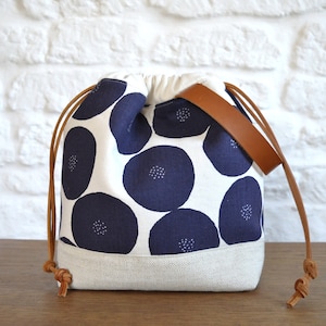 May include: A white drawstring bag with a navy blue floral pattern and brown leather straps. The bag has a white canvas bottom.