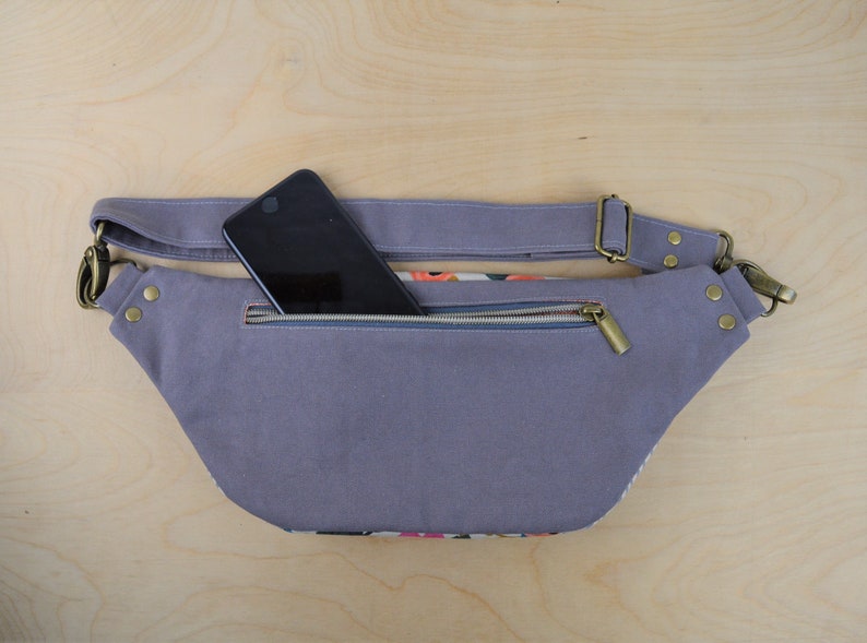 May include: A gray canvas fanny pack with a zippered pocket and a black smartphone inside. The fanny pack has a brown adjustable strap with a metal buckle.