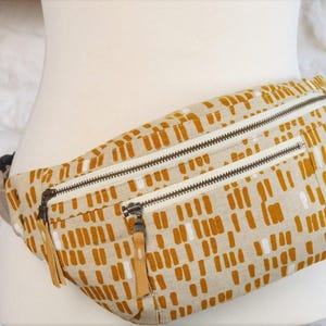 May include: A beige fanny pack with a brown and white geometric pattern. The pack has two zippered compartments.