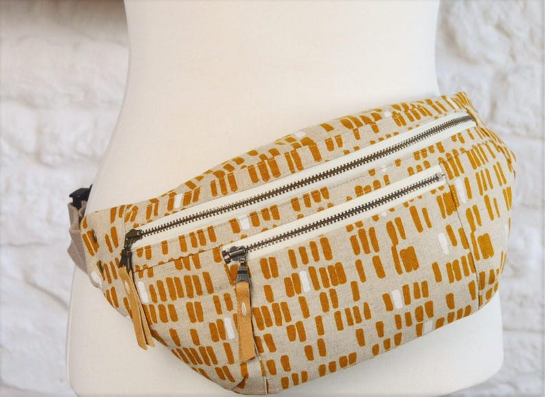 May include: A beige fanny pack with a brown and white geometric pattern. The pack has two zippered compartments.